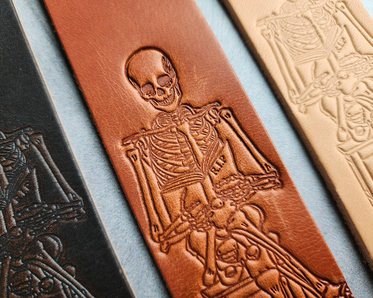 leather bookmark with a skeleton holding a book labeled R.I.P. it is a happy skeleton. 